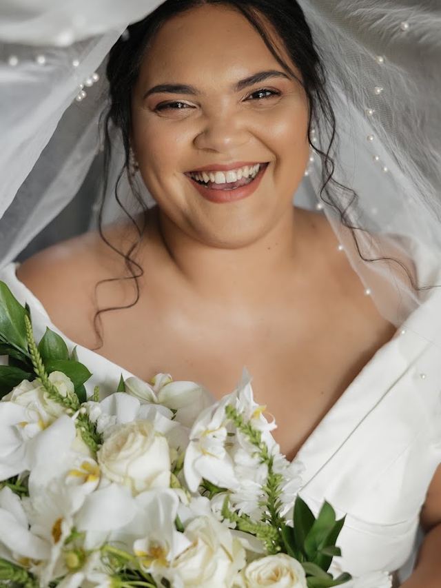 Laughing bride under a pearl-trimmed veil, holding white roses and orchids, glowing skin and soft lip