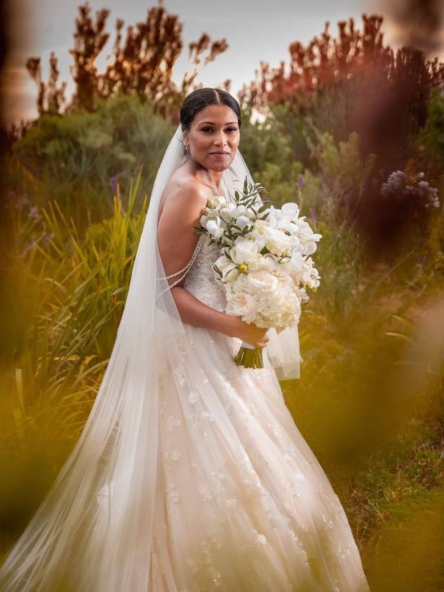 Bride in a long veil holding a white rose and orchid bouquet, sleek centre-parted updo and natural makeup
