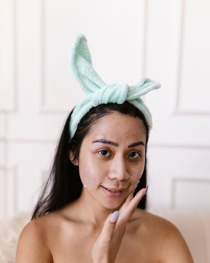 Woman in a mint headband applying skincare to her cheek