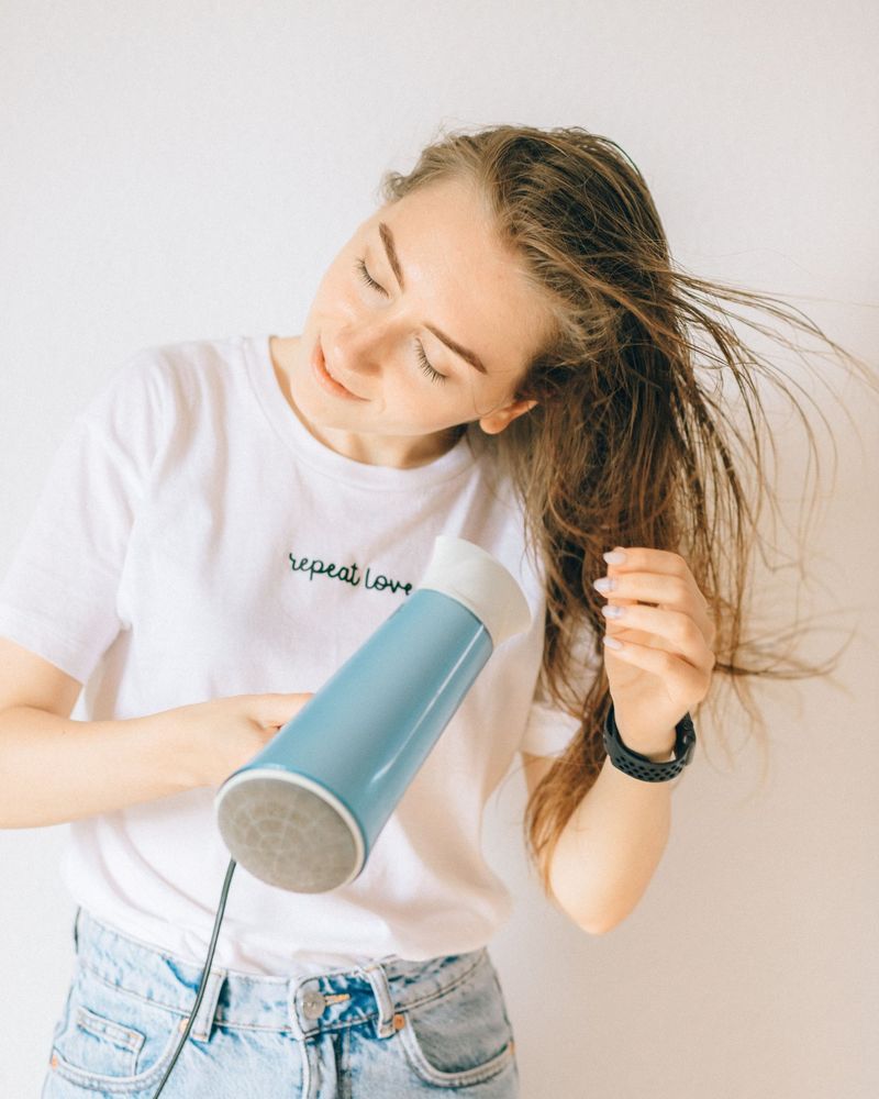 Smiling woman with her eyes closed blow-drying her long hair with a blue hairdryer