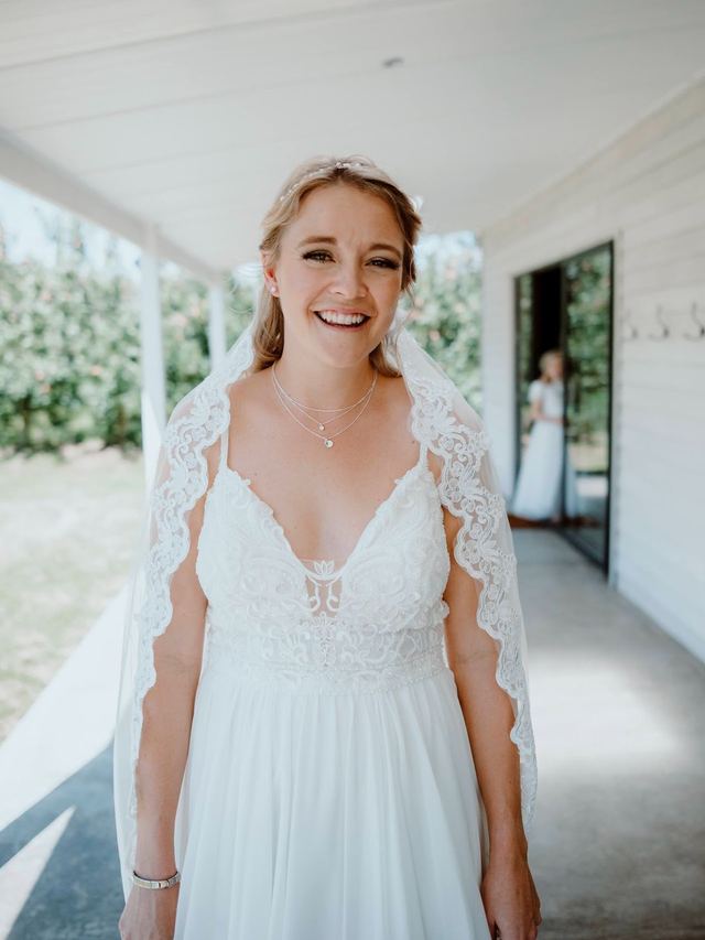 Smiling bride in a lace-edged veil on a veranda, soft natural makeup and a pearl hair vine