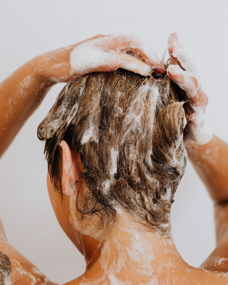 Woman washing her hair, seen from behind, working shampoo into a lather