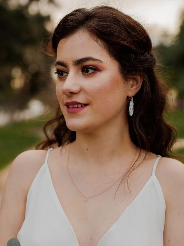 Bride looking away with soft rosy makeup and a loose half-up wave, wearing leaf earrings