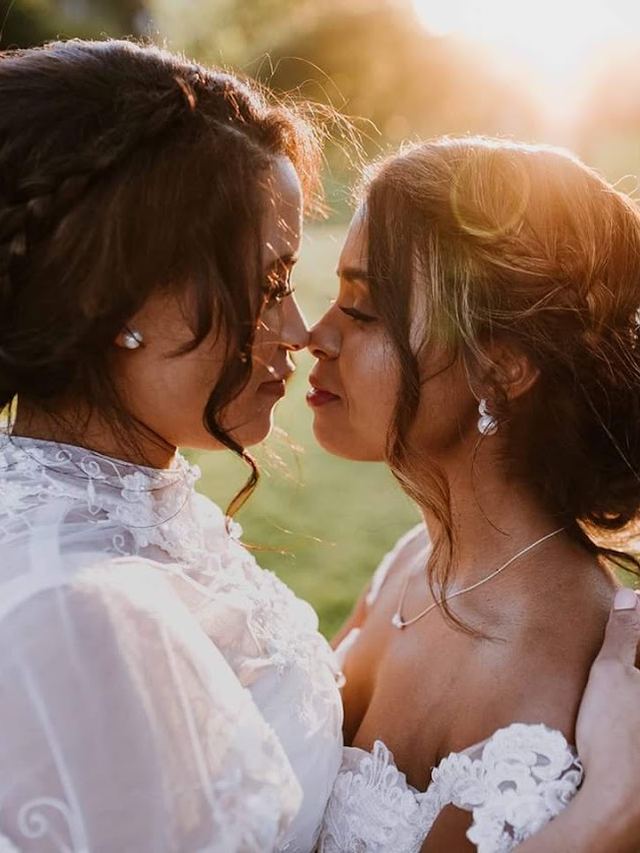 Two brides sharing a tender moment in golden light, both with romantic braided updos