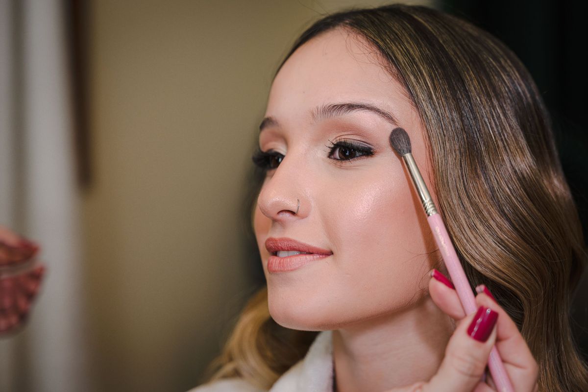 Makeup artist blending soft neutral eyeshadow with a pink brush on a woman during a bridal makeup trial